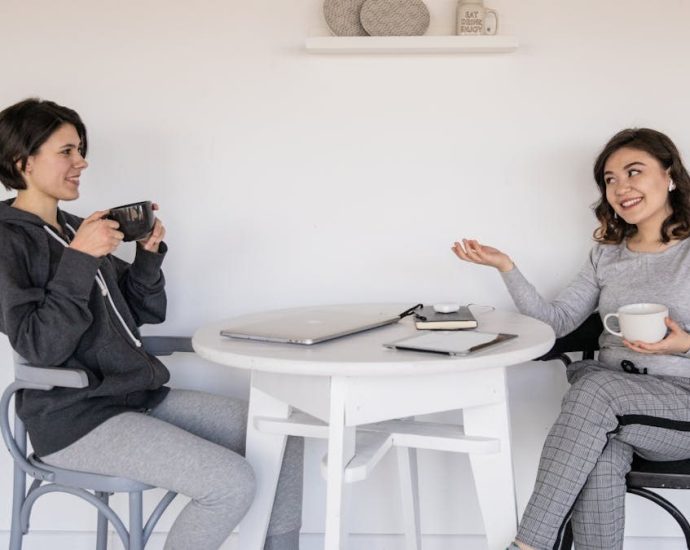 Two women enjoying a friendly chat over coffee indoors, relaxed and smiling.