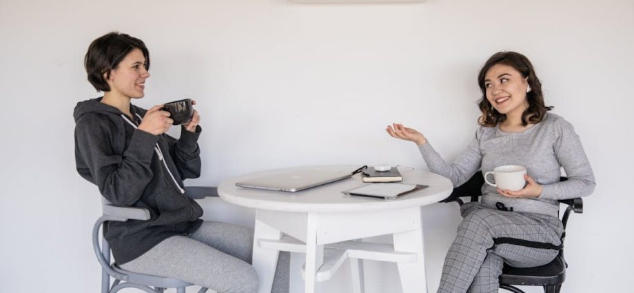Two women enjoying a friendly chat over coffee indoors, relaxed and smiling.